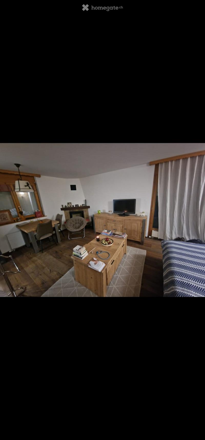 A cozy living room with a fireplace, a sofa, a coffee table, a dining area with a table and chairs, and a television on a wooden cabinet.