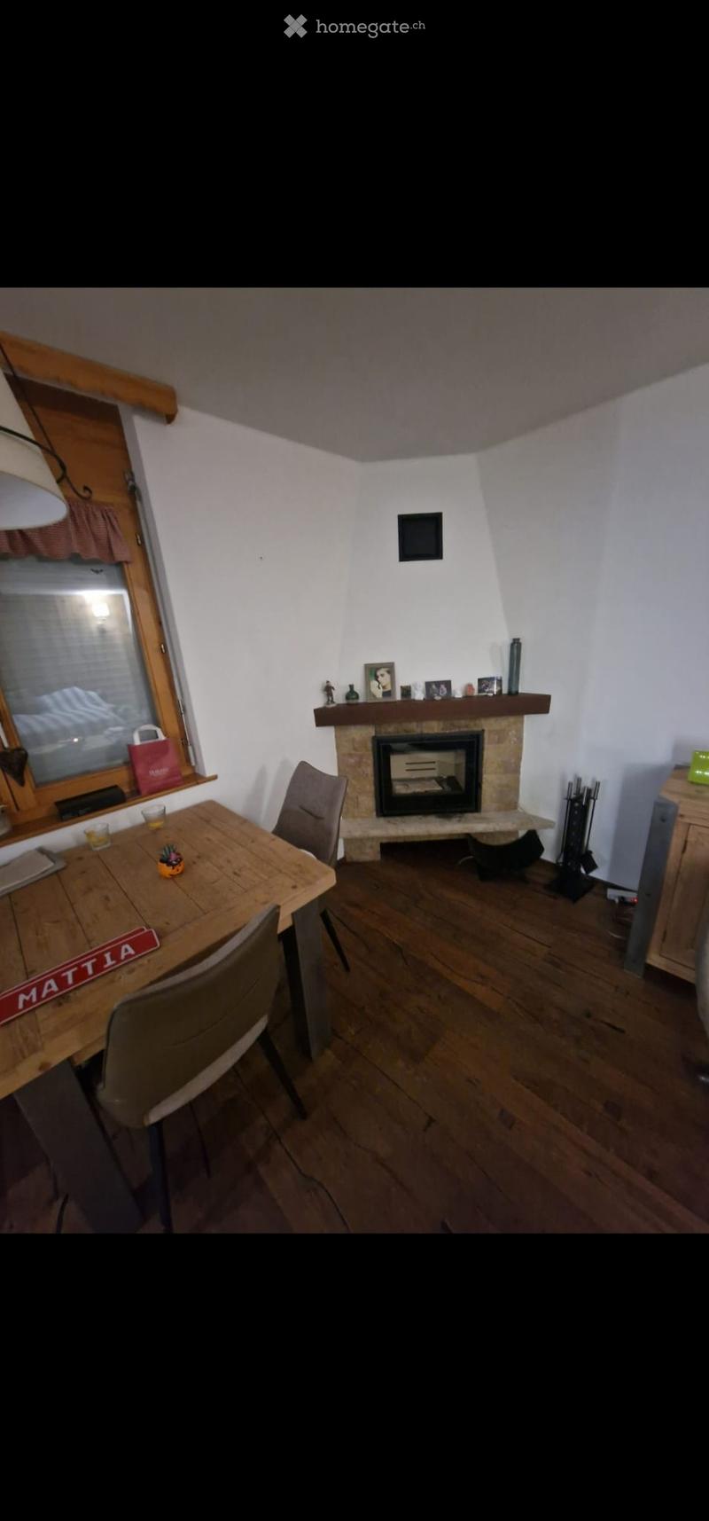Cozy living room with wooden floor, fireplace, dining table, chairs, and decorative items on the mantel.