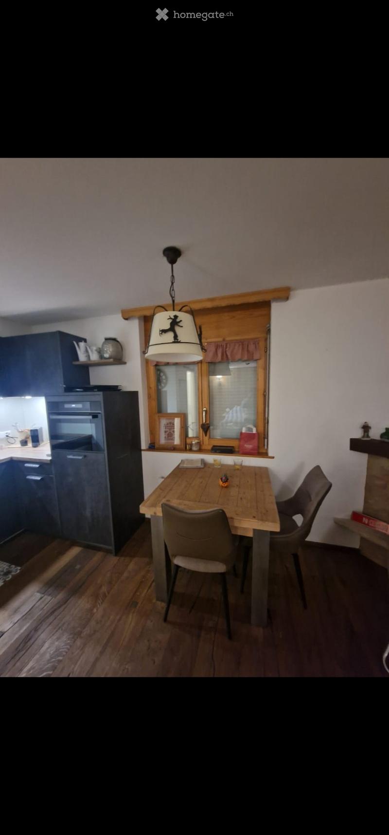 Dining area with wooden table and chairs, modern kitchen cabinets, refrigerator, and a window with a view.