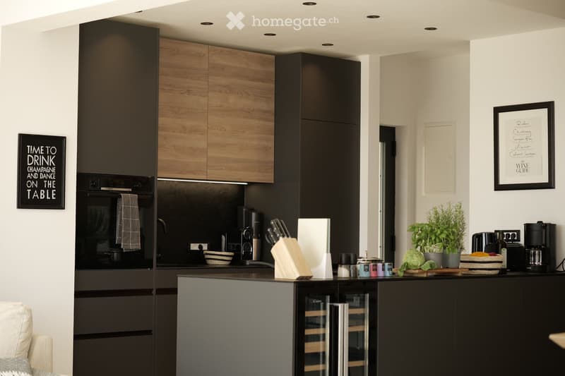 Modern kitchen with dark wooden cabinets, stainless steel appliances, and a central island. Features include a refrigerator, oven, coffee maker, knife block, and decorative items such as a plant and framed artwork.