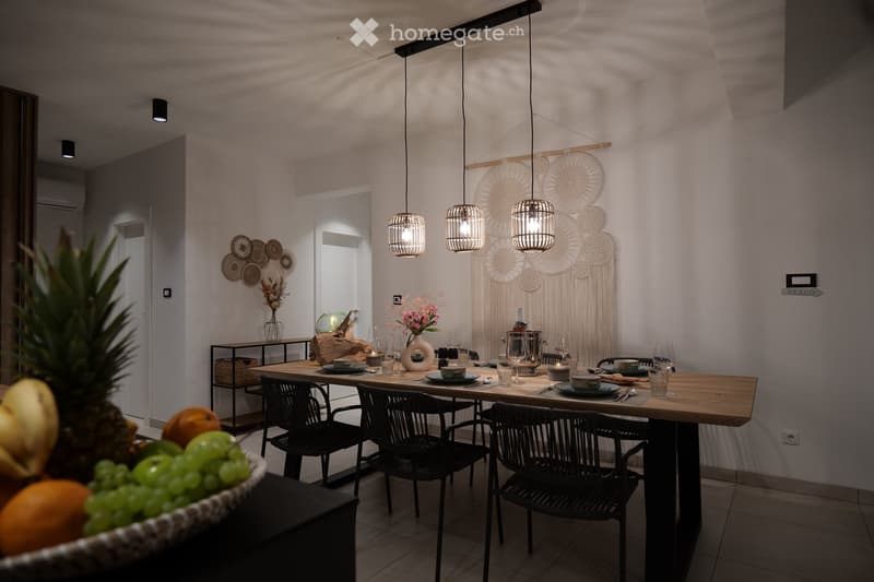 Modern dining area with a wooden table, black wicker chairs, decorative wall art, and pendant lights.