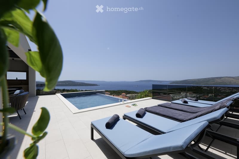 A modern rooftop terrace with a swimming pool, sun loungers, and a stunning sea view.