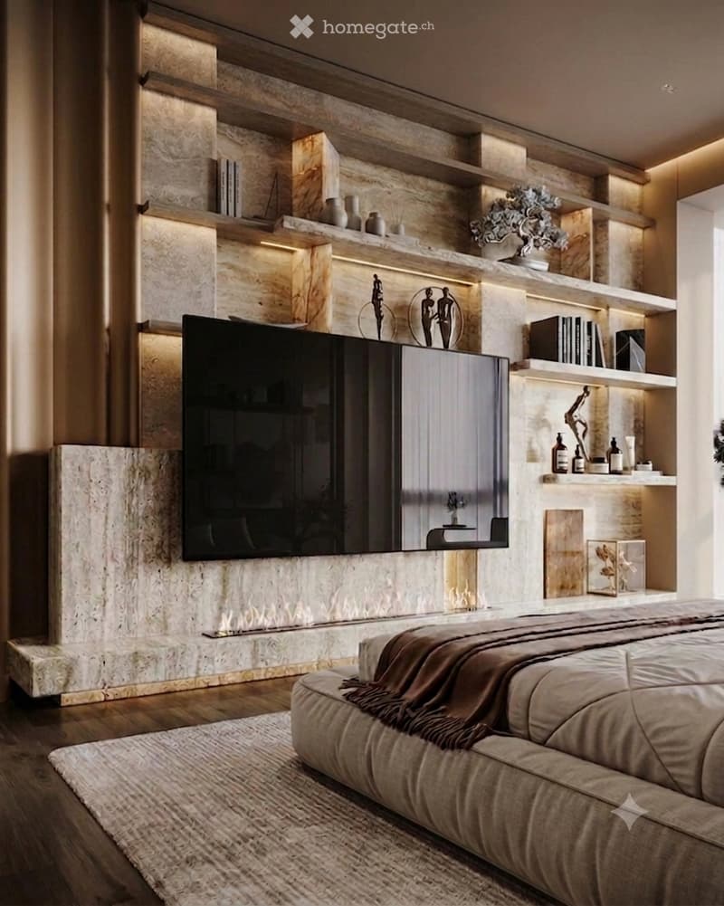Modern living room with a large flat-screen TV mounted on a stone wall, built-in shelving, a comfortable sofa, and decorative items including vases and sculptures.