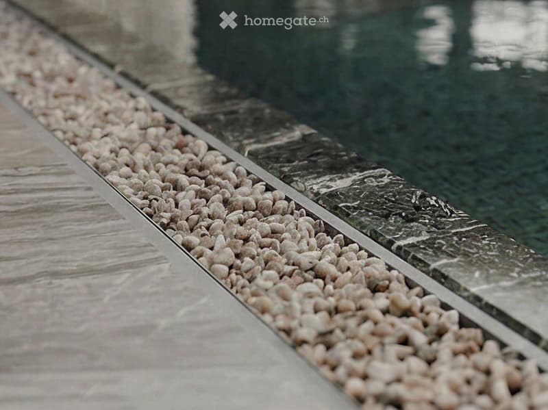 A close-up view of a water feature with a marble edge and a bed of small, smooth pebbles lining the water's edge.
