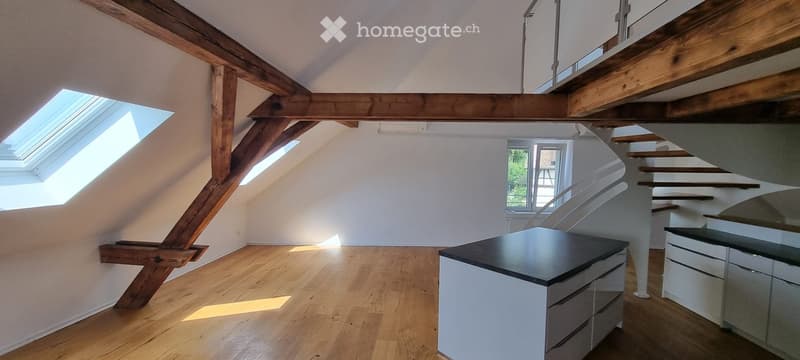 Bright attic space with wooden beams, skylights, and a small kitchen area with cabinets and a countertop.