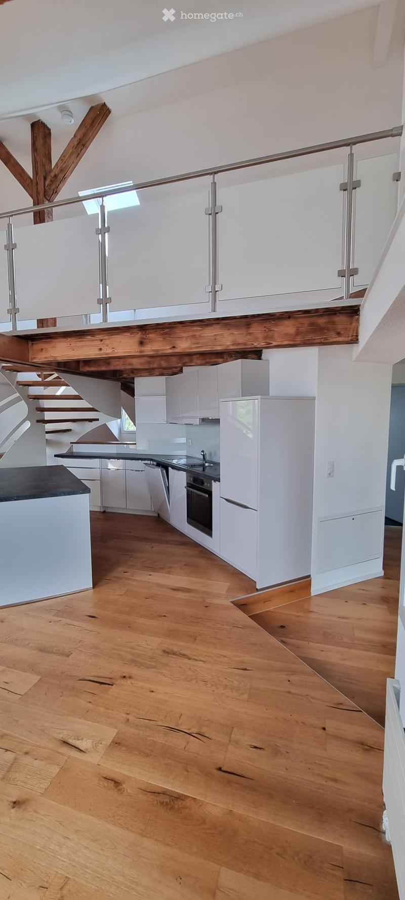 Modern kitchen with white cabinets, wooden floor, black countertop, stainless steel sink, and built-in oven and fridge.