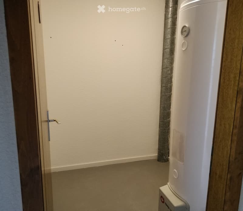 Unfurnished Room. Empty room with light-colored walls and a white appliance, likely a water heater, positioned against the wall. The door is slightly ajar, revealing a glimpse of another room.