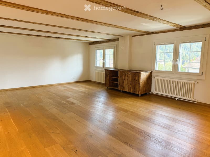 Empty room with wooden flooring, exposed wooden beams on the ceiling, and a single wooden cabinet against the wall.