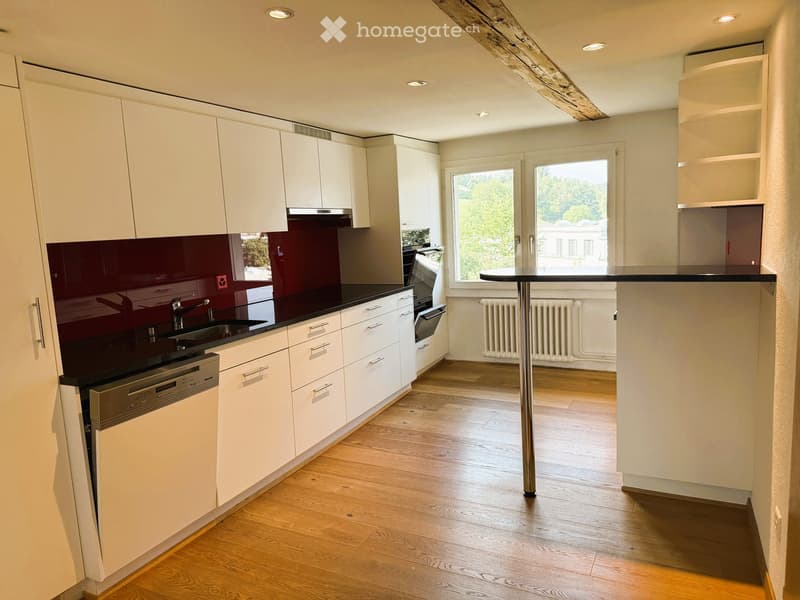 Modern kitchen with white cabinets, dark countertops, stainless steel appliances, and wooden flooring.