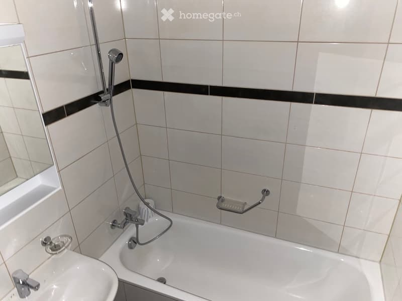 Bathroom with a bathtub, sink, and showerhead, featuring tiled walls and a handrail for safety.
