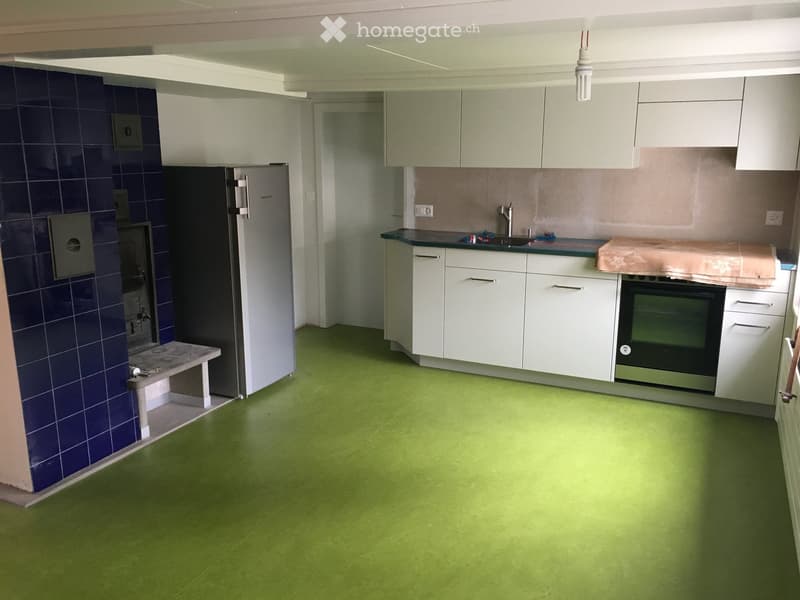 Modern kitchen with white cabinets, green flooring, stainless steel appliances, and a small bench near the wall.