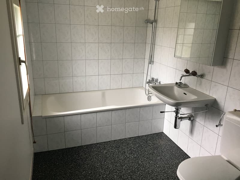 Bathroom with tiled walls, bathtub, sink, toilet, and a window providing natural light.