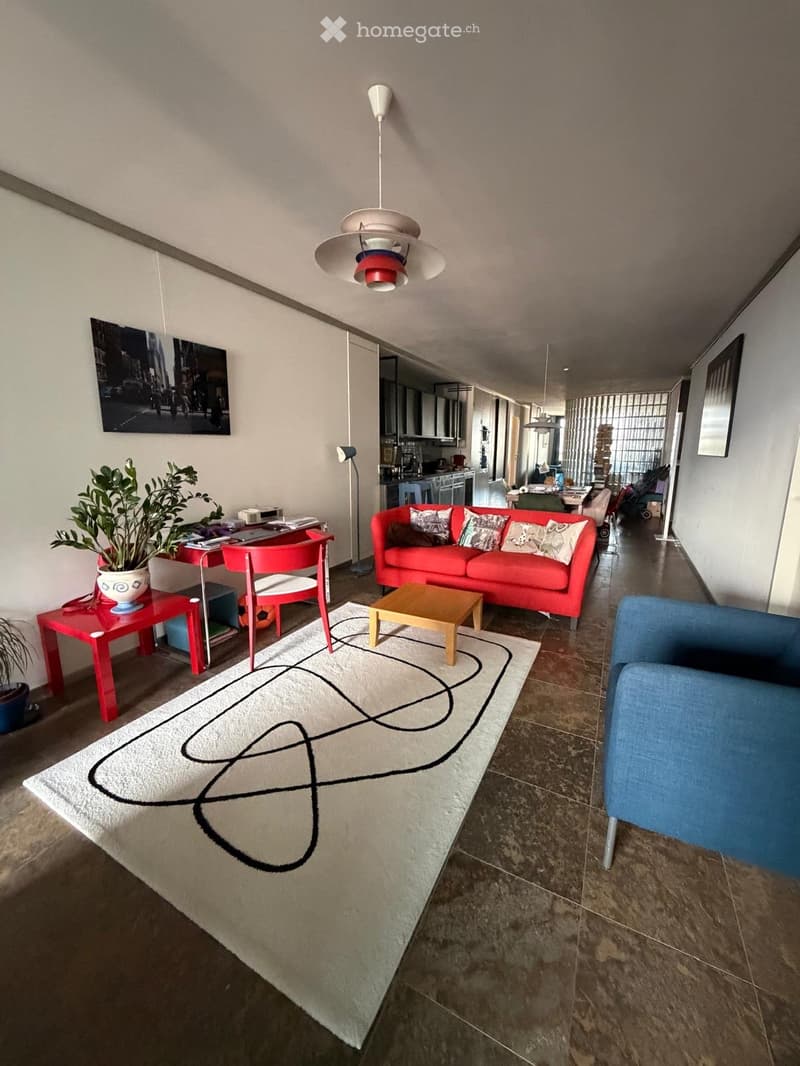 Modern living room with a red sofa, coffee table, blue armchair, red side table, potted plant, and a large abstract rug on the floor.