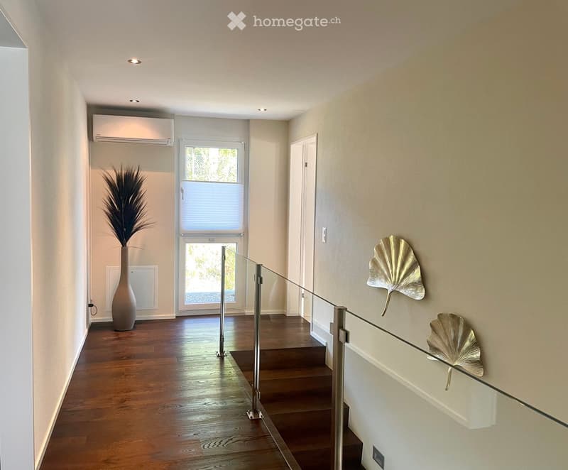 Entryway with wooden floor, wall mounted AC, decorative fan leaves, and a glass railing on stairs