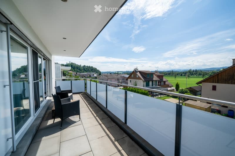 balcony, chairs, glass railing, tiled floor, overlooking a landscape with fields and houses