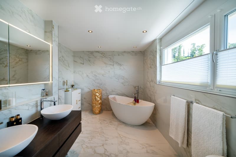 white marble tiles, two vanity sinks, freestanding bathtub, golden vase, marble wall, large window, towel racks