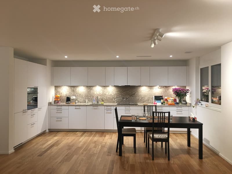 Modern kitchen with white cabinets, wooden flooring, and a dining area with a black table and chairs.
