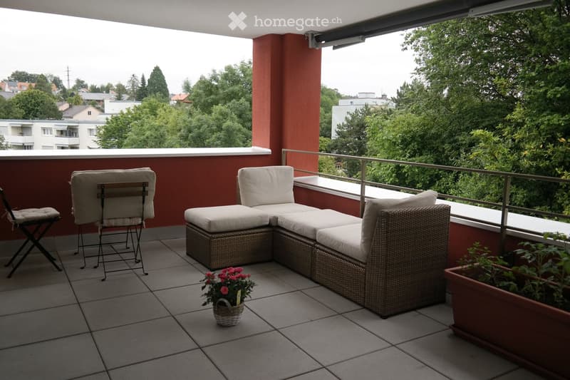 Balcony with a modern seating area, including a wicker sofa, two chairs, a small table, and potted plants.