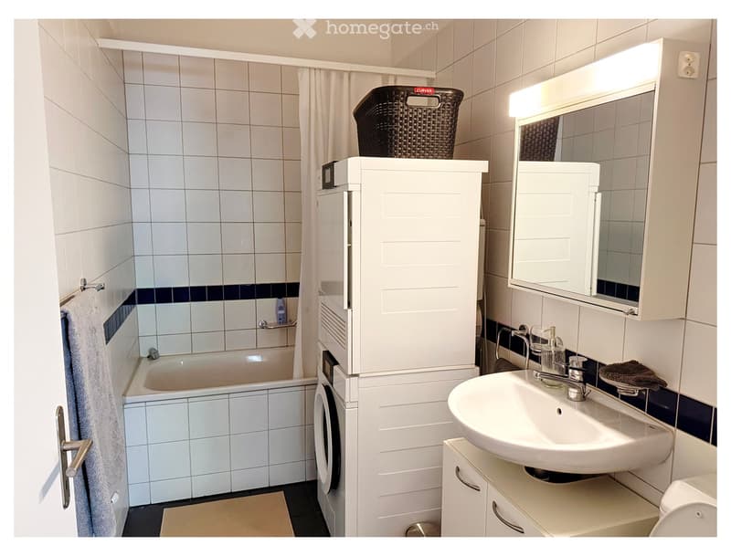 Modern bathroom with white tiles, a bathtub, a sink with a mirror cabinet, and a wicker basket on top of a cabinet.
