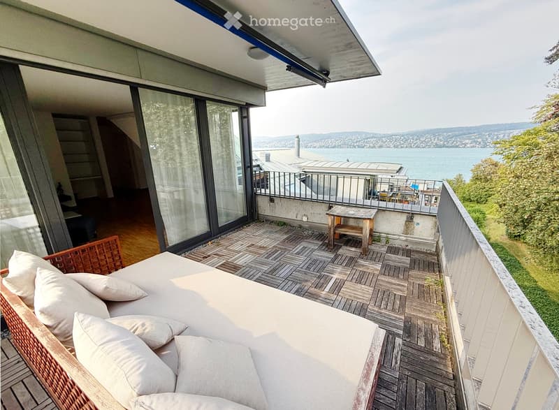Balcony with wooden decking, white sofa, small wooden table, scenic water view.