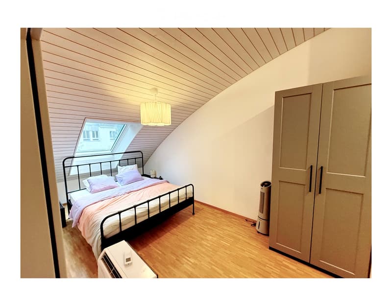 Cozy attic bedroom with wooden floors, slanted wooden ceiling, skylight window, bed with pink bedding, nightstand, and air conditioner units.