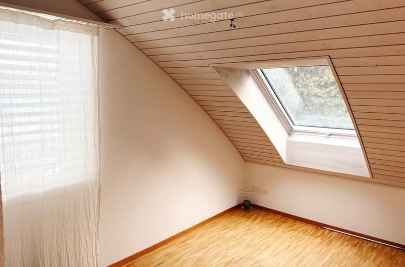 Empty attic room with wooden floor, white walls, skylight window, and a small decorative candle on the floor.
