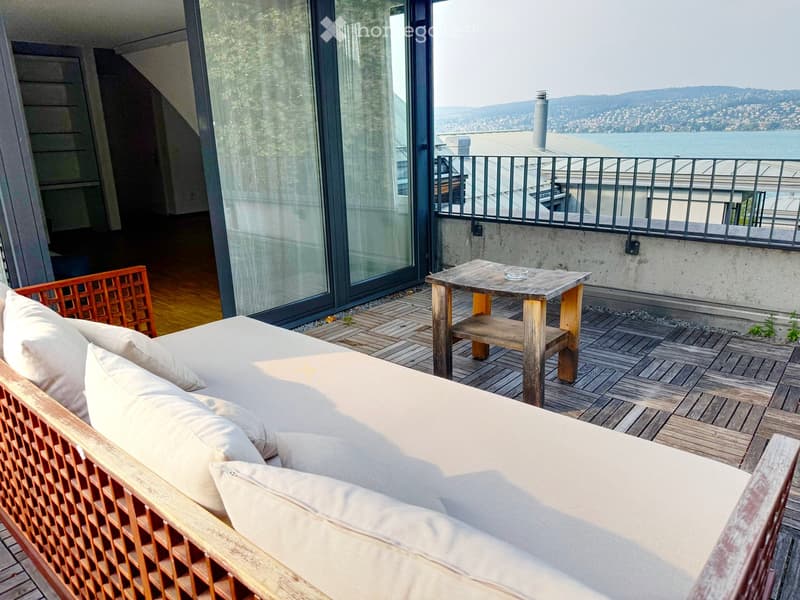 Balcony with wooden decking, white sofa, small wooden table, scenic view of water and hills.