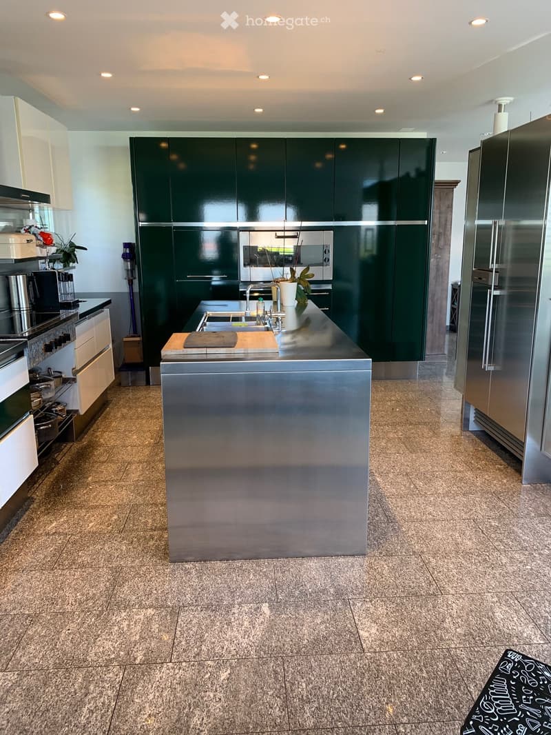 Modern kitchen with a stainless steel island, green cabinets, and a marble floor.
