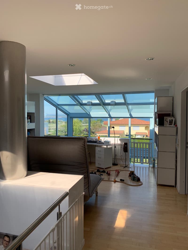 A room with a desk, chair, lamp, and a view of the outside through large windows.