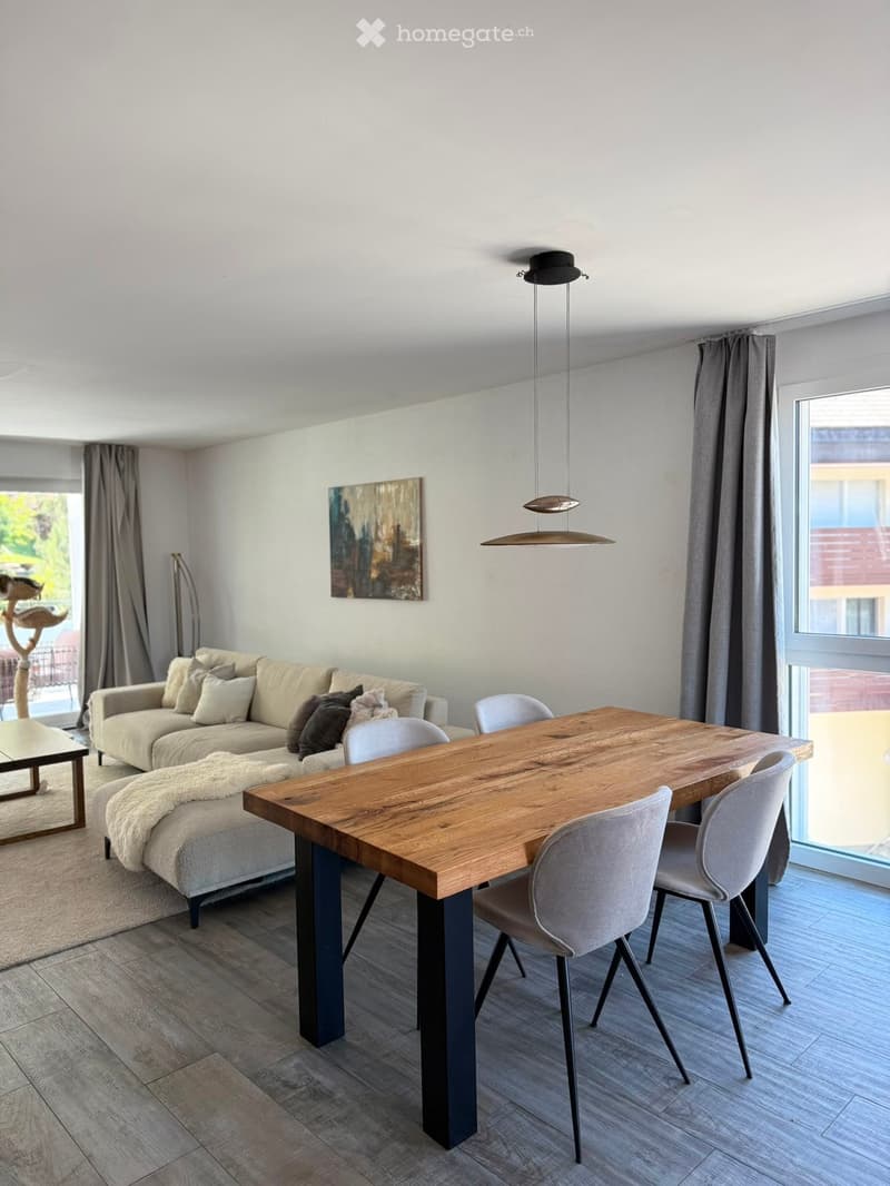 Modern living and dining area with a beige sofa, wooden dining table, grey chairs, floor lamp, and artwork on the wall.