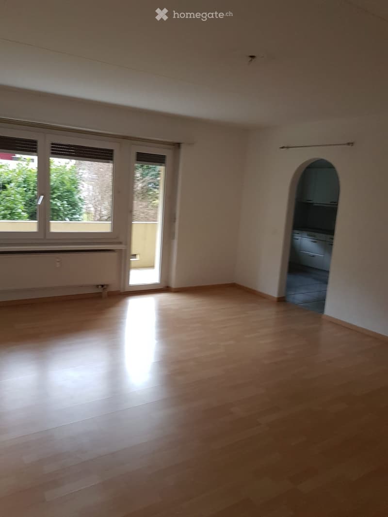 Empty room with wooden flooring, large windows, and a sliding glass door leading to a balcony.