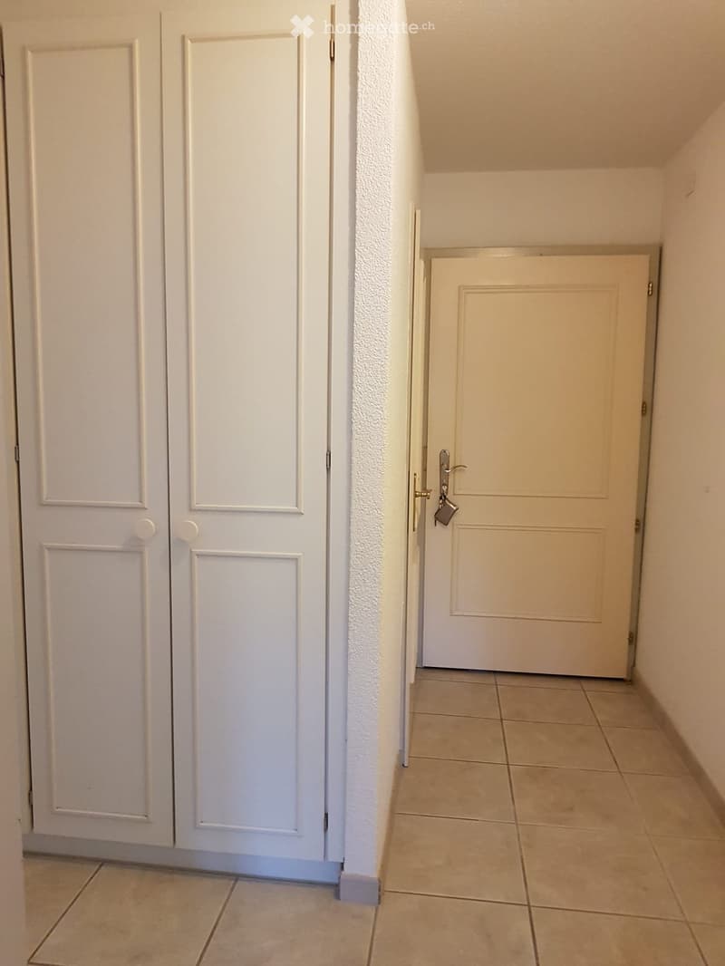 A narrow hallway with tiled flooring, white walls, and two doors: a double door on the left and a single door on the right.