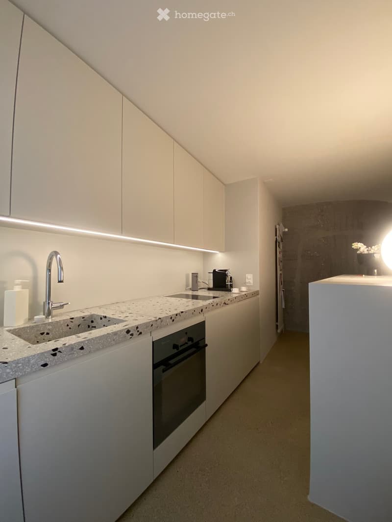 Modern kitchen with white cabinets, a marble countertop, a sink with a modern faucet, and an oven. A coffee maker and a cup are placed on the counter.