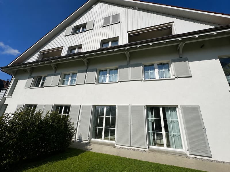 Two-story house with white siding, multiple windows with shutters, and a balcony on the upper level.