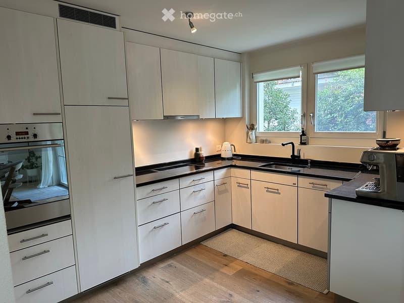 Modern kitchen with white cabinets, wooden flooring, stainless steel oven, sink, and coffee machine on the counter.