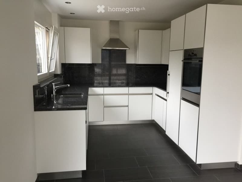 Modern kitchen with white cabinets, black countertops, and black tiled flooring. Features a stainless steel range hood, sink, and oven.