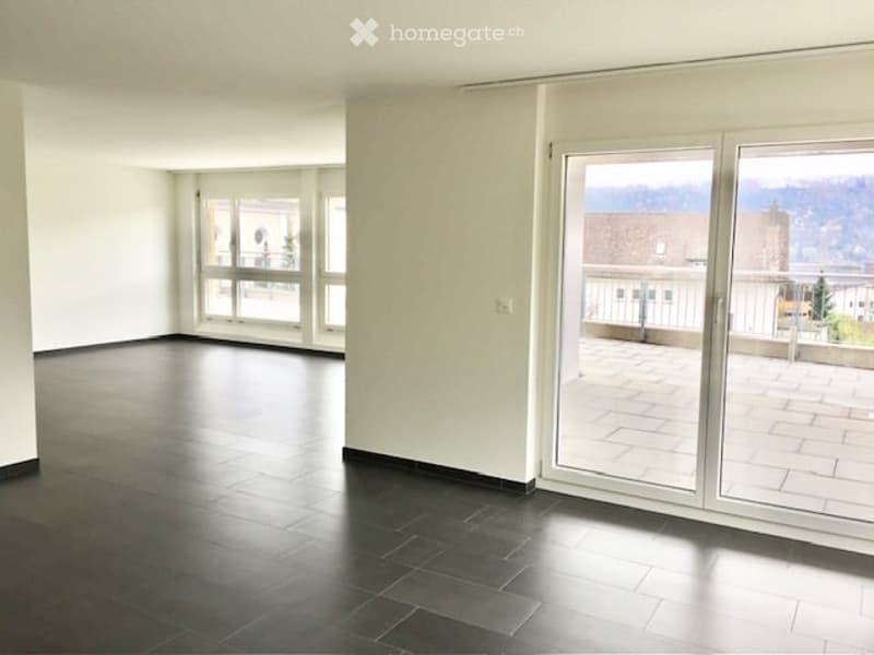 Empty room with dark tiled floor, white walls, large windows, and sliding glass doors leading to a balcony.