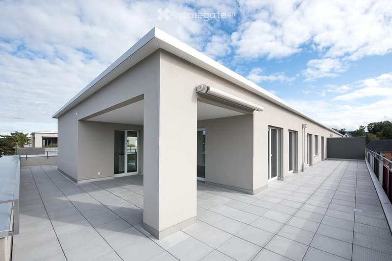 Modern single-story building with a flat roof, large windows, and a covered entrance area. The building is light grey with clean lines and a contemporary design.