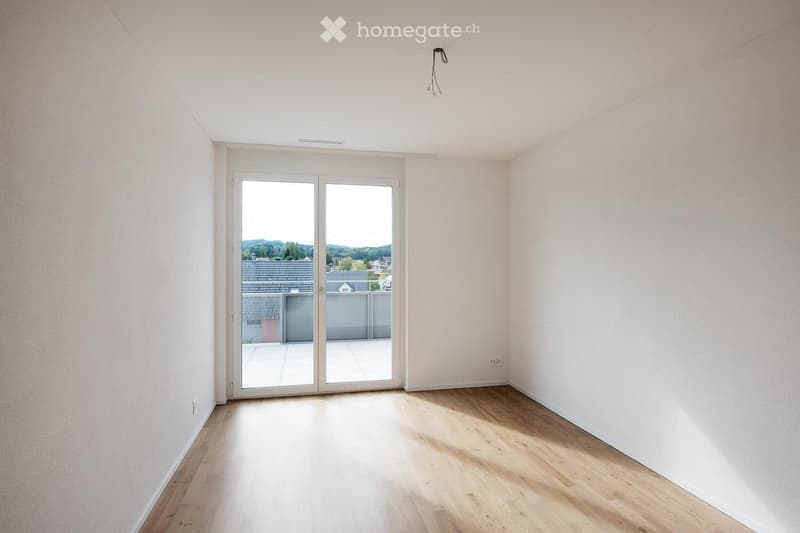 Empty room with light wooden flooring, white walls, and a large sliding glass door leading to a balcony.