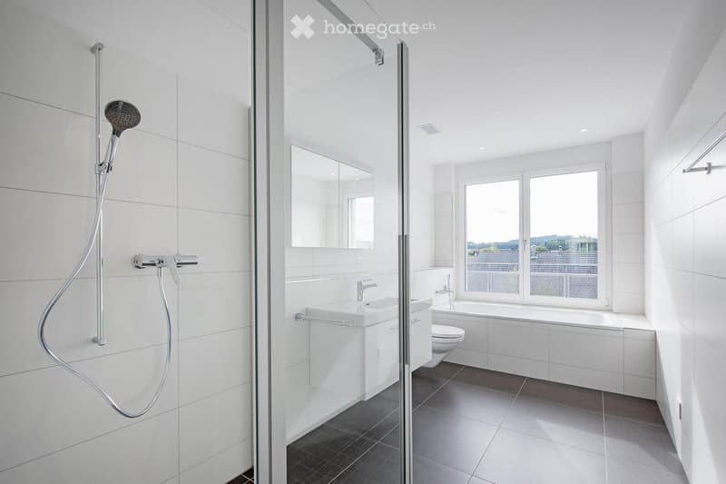 Modern bathroom with white tiles, a glass-enclosed shower, a sink, a toilet, and a bathtub, featuring large windows with a view.