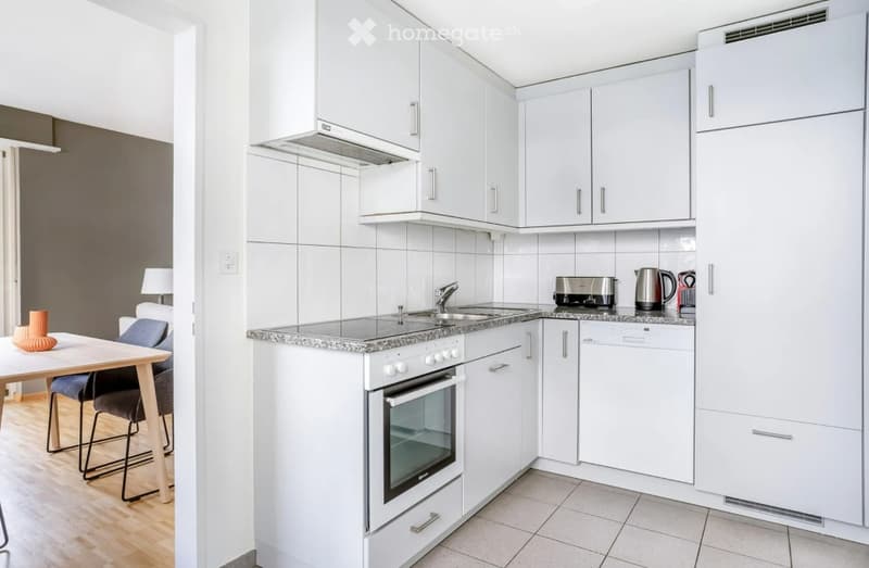 Modern kitchen with white cabinets, stainless steel appliances, and a small dining area with a table and chairs.