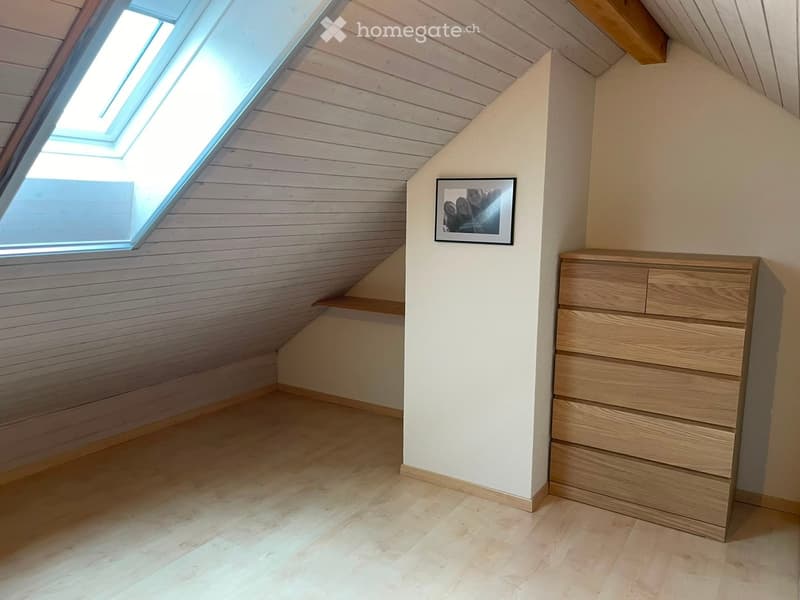 Attic room with wooden walls, slanted ceiling, skylight window, and a chest of drawers.