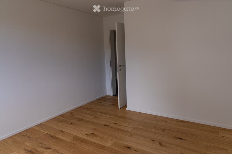 Empty room with light-colored walls and wooden flooring, featuring an open doorway leading to another space.