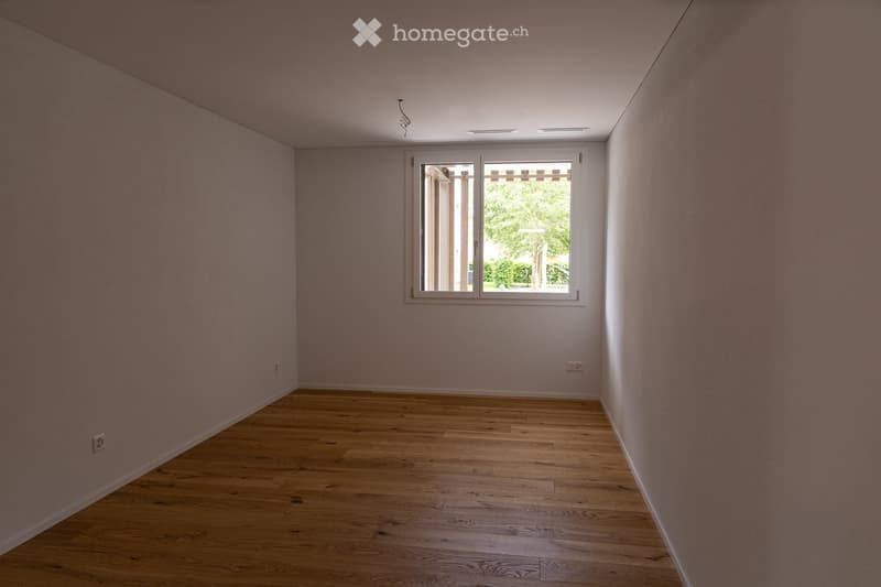 Empty room with light pink walls and wooden flooring, featuring a single window with white frame and blinds.