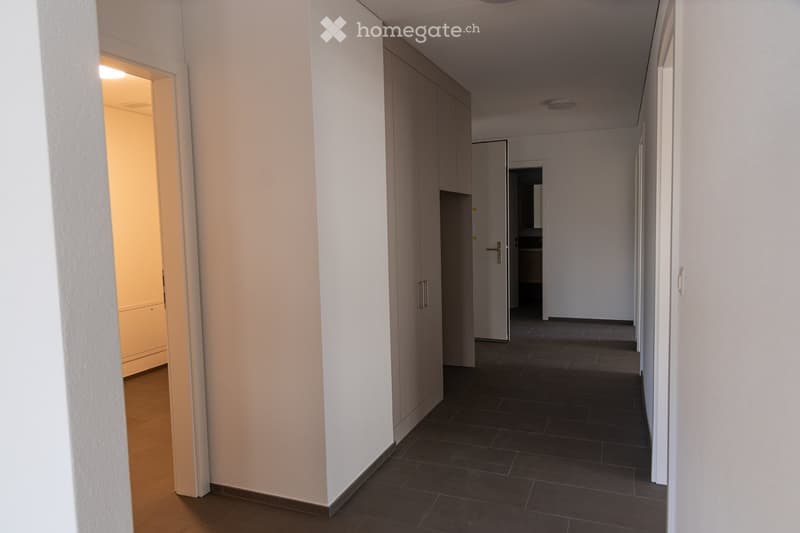 Empty hallway with white walls, dark tiled floor, and several closed doors leading to other rooms.
