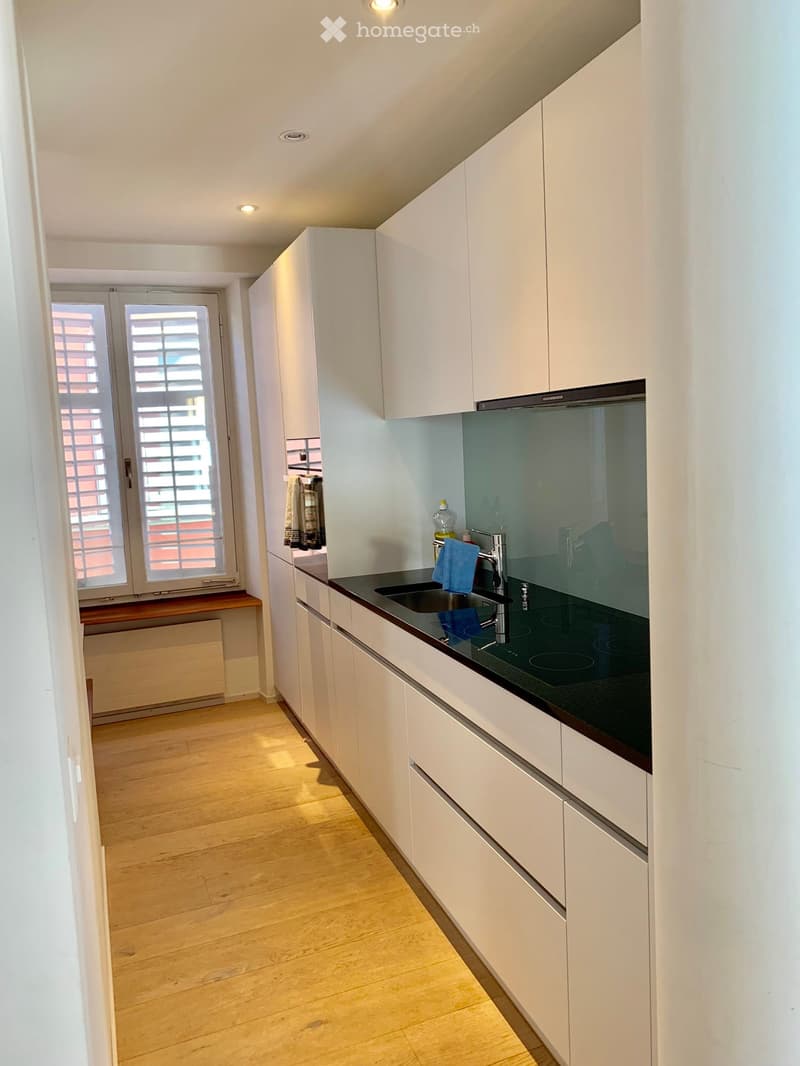 Modern kitchen with white cabinets, black countertop, and wooden flooring. Features a sink, faucet, and a bottle on the counter.