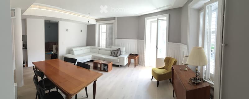 Bright living room with white sectional sofa, wooden dining table, green armchair, and decorative lamps.