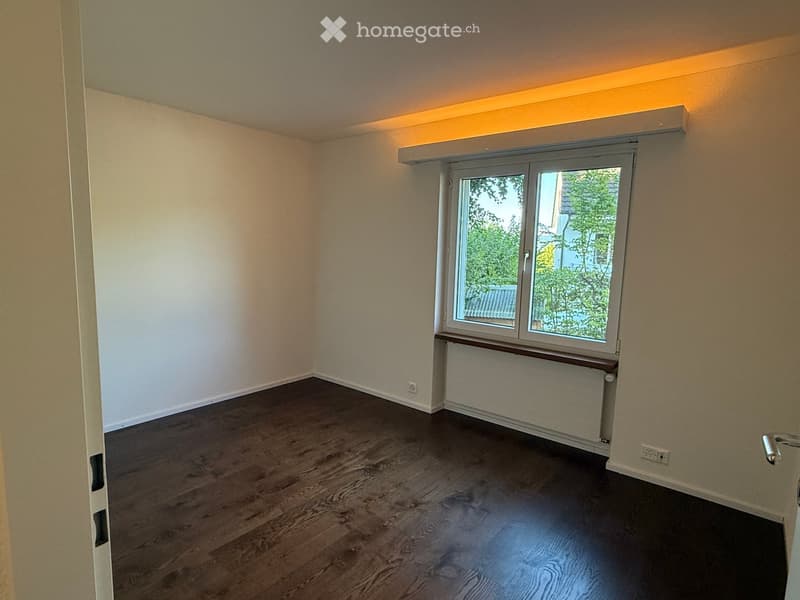 Empty room with wooden flooring, white walls, and a large window with a radiator below it.
