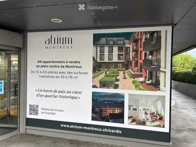 Promotional signboard for "atrium MONTREUX" advertising 44 apartments for sale in the center of Montreux, featuring images of residential buildings, balconies, and interior spaces.