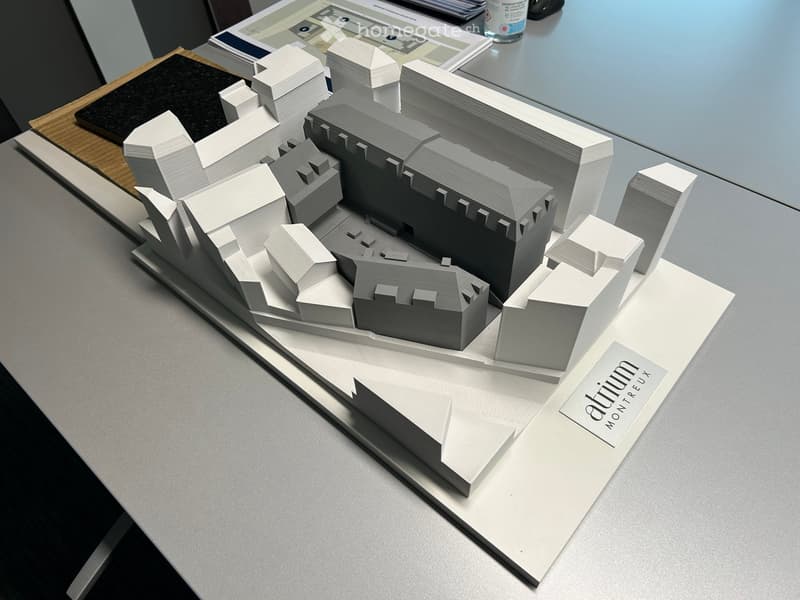 Architectural model of a building with detailed geometric shapes and structures, displayed on a table with architectural drawings and materials.